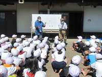 昭和小の生徒達が稲の植え方の説明を聞いている様子の写真