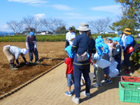 管理組合員が久保田保育所の園児達にさつまいもの掘り方を説明している様子の写真